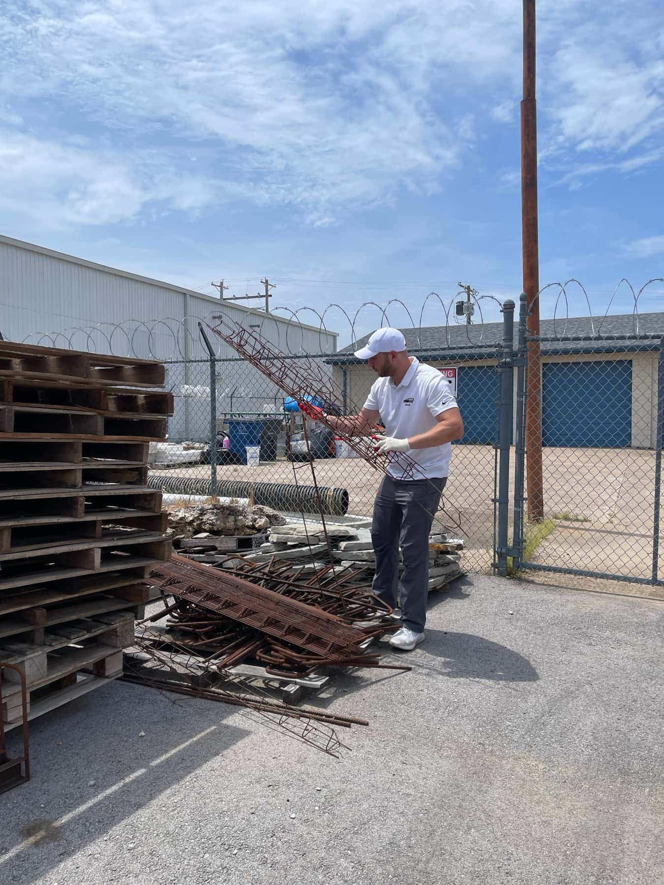Victor sorting lengths of rebar and steel mesh at a fenced Tulsa scrap yard beside a stack of pallets
