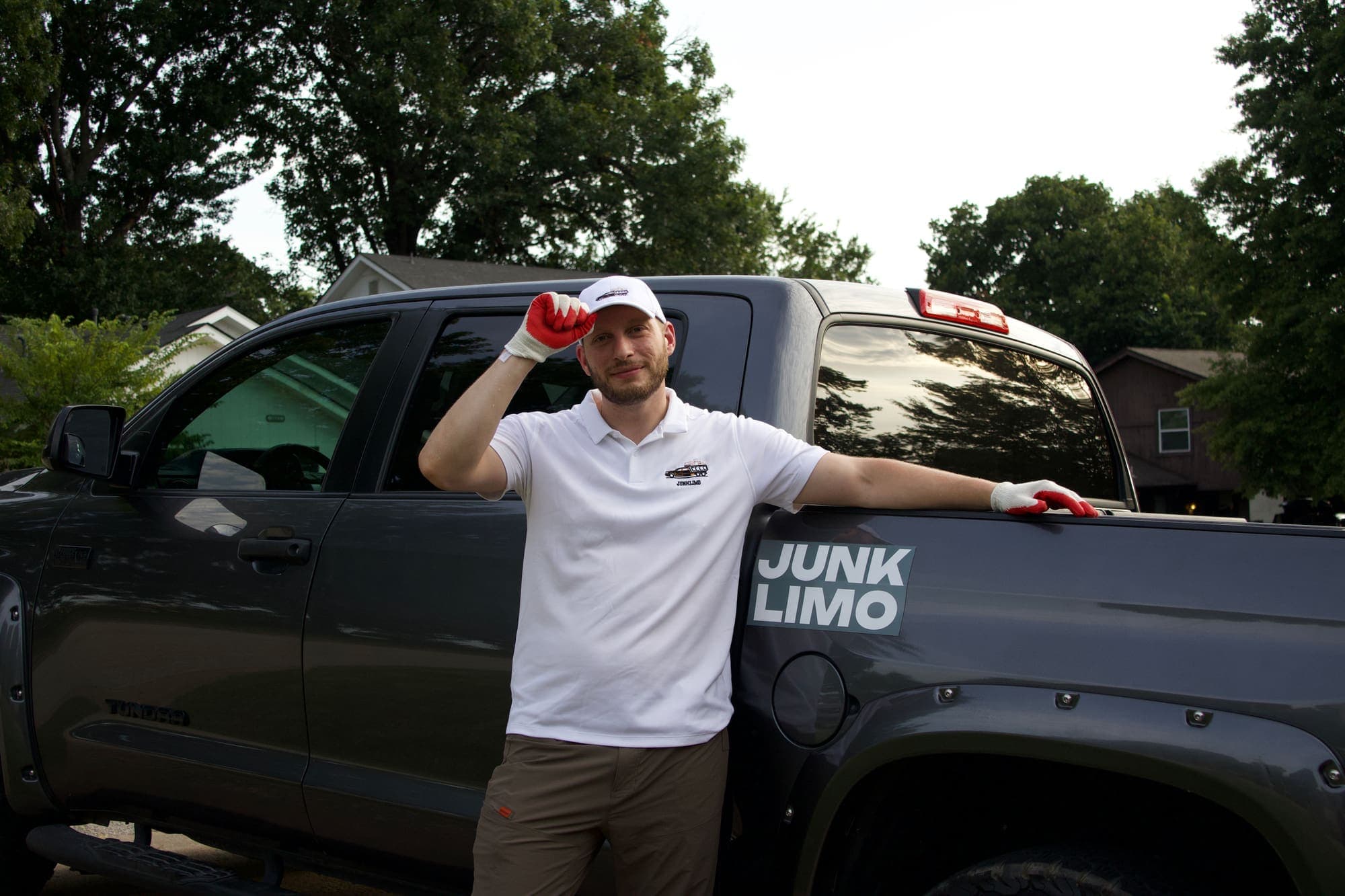 Victor leaning against the bed of his pickup truck beside the JUNK LIMO decal, touching the brim of his cap