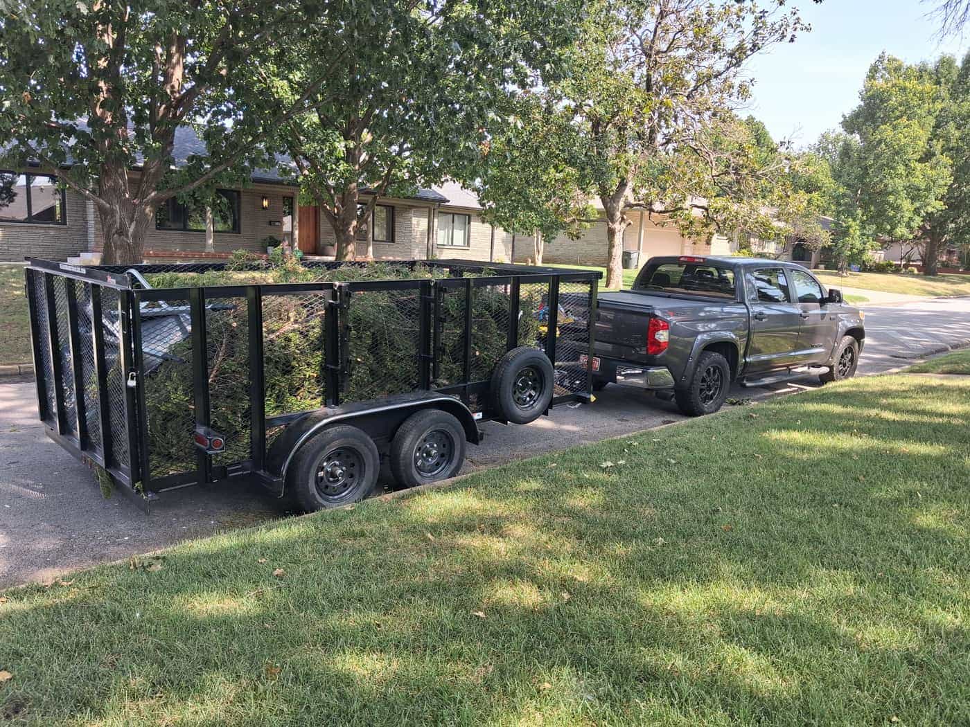The JunkLimo trailer heaped with branches and brush, hitched to the truck outside a Tulsa ranch house