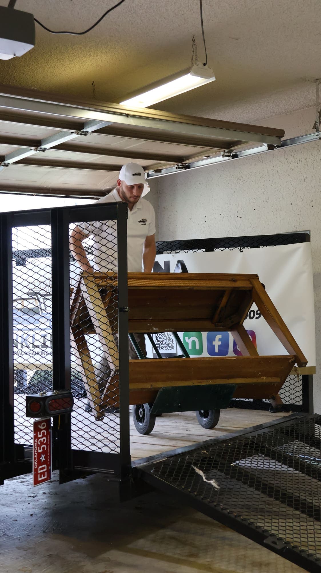 Victor guiding a large wooden cabinet on a hand truck up the ramp of the JunkLimo trailer