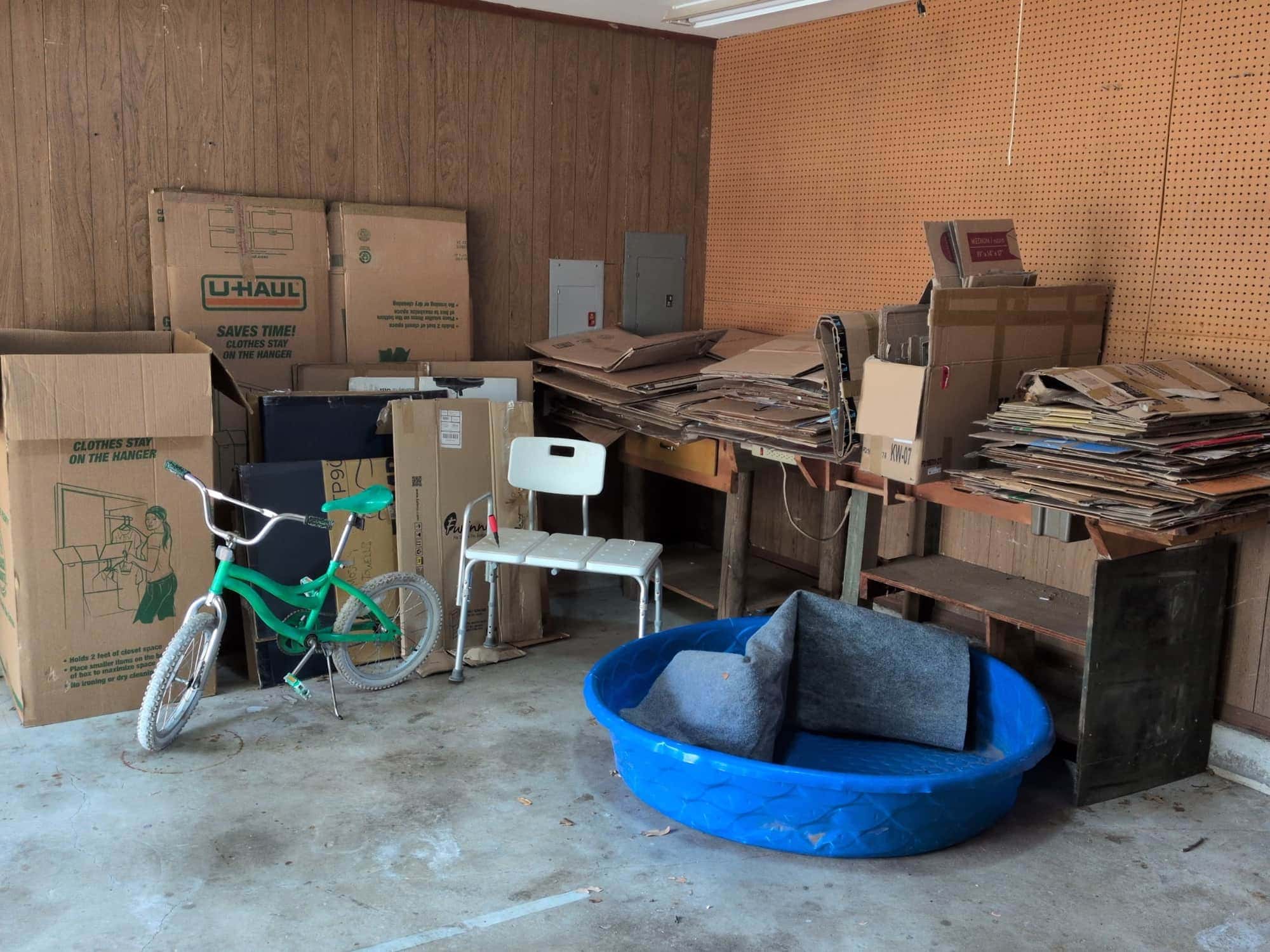 A Tulsa garage packed with moving boxes, stacks of flattened cardboard, a child’s bike, a shower bench and a paddling pool before a cleanout