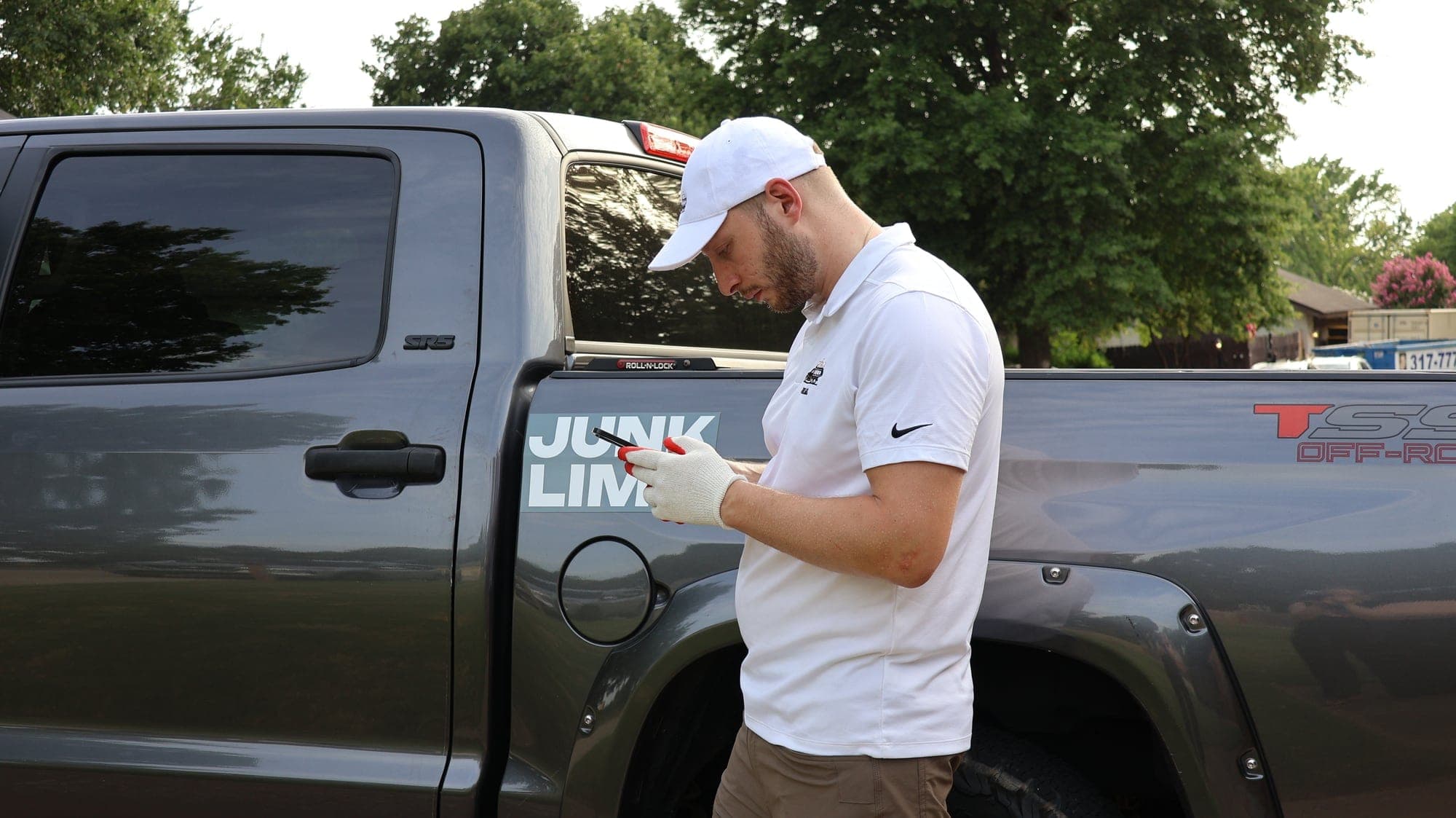Victor standing at the side of his grey pickup truck looking at his phone, with the JUNK LIMO door decal beside him